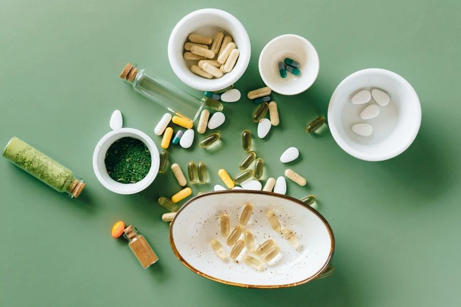Gélules et poudres de compléments alimentaires disposées dans des coupelles sur un fond vert