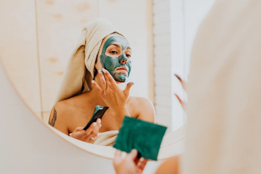 Femme avec un masque à l’argile verte sur le visage, cheveux enveloppés dans une serviette
